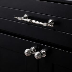 May include: Close-up of black cabinet doors with silver hardware. The top door features a silver handle, while the bottom doors have two silver ball knobs. The hardware contrasts with the dark wood.