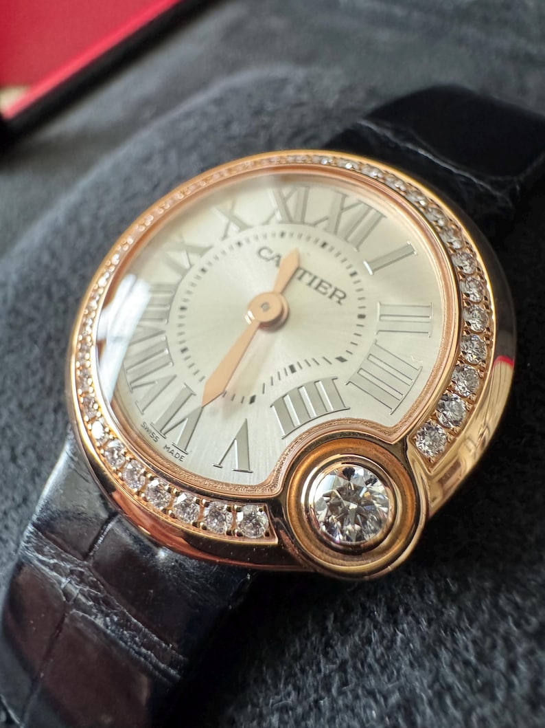 Puede incluir: Reloj de lujo con caja de oro rosa y esfera blanca con n&uacute;meros romanos. El reloj tiene un bisel con diamantes y un diamante grande a las 6. Se presenta sobre una correa de cuero negro.