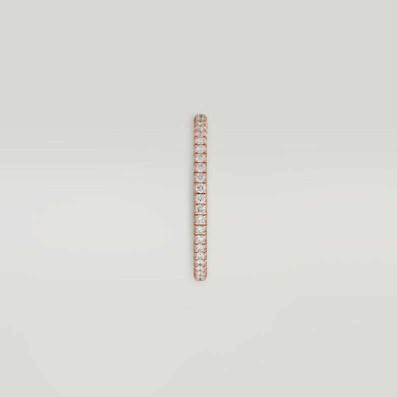 Puede incluir: Un anillo de oro rosa con una fila continua de peque&ntilde;as piedras preciosas transparentes. El anillo est&aacute; sobre un fondo neutro, resaltando el brillo de las piedras. El dise&ntilde;o es simple y elegante.