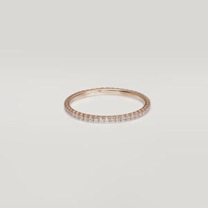 Puede incluir: Un anillo de eternidad de oro rosa con una fila continua de peque&ntilde;as piedras preciosas transparentes. El anillo se muestra sobre un fondo blanco liso, resaltando su delicado dise&ntilde;o y brillo. Este anillo es una joya fina.
