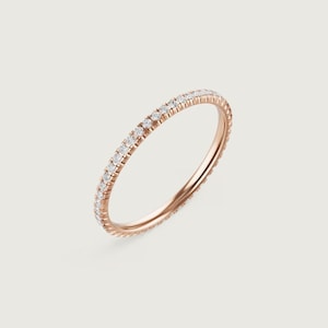 Puede incluir: Anillo de oro rosa con una banda completamente engastada con peque&ntilde;as piedras preciosas claras. El anillo se muestra sobre un fondo suave y neutro, resaltando su delicado dise&ntilde;o. Las piedras preciosas brillan, agregando un toque de elegancia.