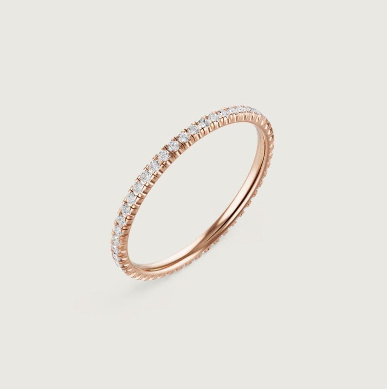 Puede incluir: Anillo de oro rosa con una banda completamente engastada con peque&ntilde;as piedras preciosas claras. El anillo se muestra sobre un fondo suave y neutro, resaltando su delicado dise&ntilde;o. Las piedras preciosas brillan, agregando un toque de elegancia.
