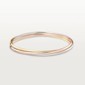 May include: Three interlocking bangles in rose gold, yellow gold, and silver. The bands are smooth and round, creating a seamless, elegant design. The jewelry is displayed on a white background.