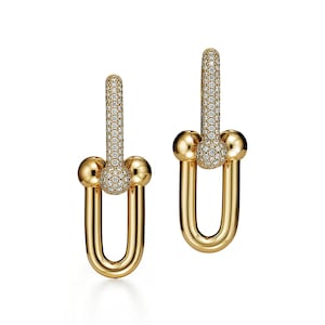 May include: A pair of gold-colored hoop earrings. The top portion of each earring is a vertical bar covered in small, sparkling stones. The bottom is a U-shaped design with a small gold ball at the top of the U.