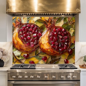 May include: A kitchen splashback panel featuring a stained glass style mosaic of two halved pomegranates with deep red seeds, golden yellow rinds, and green leaves, positioned behind a stainless steel gas range and a metallic range hood.