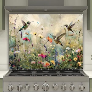 以下が含まれることがあります： キッチン用の装飾的なバックボード。活気のある花の咲く牧草地のシーンと飛んでいるハチドリが描かれています。アートワークは、ピンク、黄色、紫の色合いのカラフルな野生の花と、広げられた鳥の翼を示しています。ステンレス製のレンジの上に設置されています。