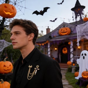 May include: A gold-toned brooch with a skull and dagger design, featuring dangling chains, is pinned to a black blazer. The background includes Halloween decorations: carved pumpkins, a haunted house, and bats.