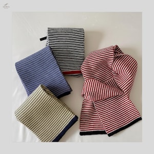 Könnte beinhalten: Vier gefaltete Schals in verschiedenen Farben: Blau, Olivgrün, Schwarz und Weiß sowie Rot und Weiß. Die Schals haben horizontale Streifen und sind aus Strickmaterial. Der rot-weiß gestreifte Schal ist entfaltet. Die Schals werden auf einer weißen Oberfläche präsentiert.
