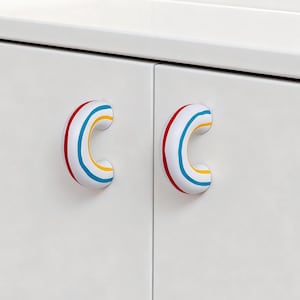 May include: White cabinet doors with two C-shaped drawer pulls. The pulls are white with red, yellow, and blue stripes. The cabinet doors are plain white.