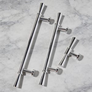 以下が含まれることがあります： 黒い持ち手と「But First, Coffee」の太字の黒い文字が入った白いセラミックマグカップ。マグカップはぼやけた背景に置かれており、居心地の良い環境を示唆しています。