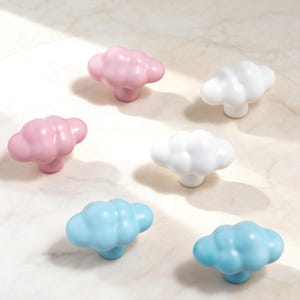 Può includere: Sei pomelli per armadi a forma di nuvola nei toni del rosa, bianco e blu. I pomelli sono realizzati in materiale lucido e sono disposti su una superficie chiara. Questi pomelli decorativi sono ideali per aggiungere un tocco stravagante ai mobili.