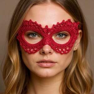 Könnte beinhalten: Nahaufnahme einer roten gehäkelten Augenmaske. Die Maske hat einen detaillierten, gewellten Rand und ein offenes Design. Die Maske bedeckt die Augen und den Nasenrücken. Die Maske ist aus weichem, strukturiertem Garn gefertigt.