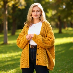 Może przedstawiać: Musztardowy kardigan z warkoczowym splotem z zapięciem na guziki. Kardigan jest noszony na białej górze i ciemnoniebieskich dżinsach. Widoczny jest brązowy pasek ze złotą klamrą. Tło to park z zieloną trawą i drzewami.