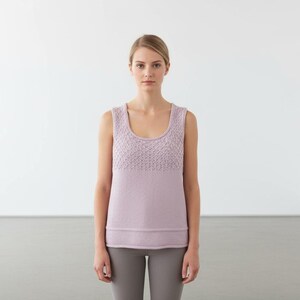 May include: A sleeveless, light purple tank top with a textured knit pattern across the upper chest. The top has a rounded neckline and a ribbed hem. The model is wearing gray leggings.
