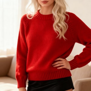Può includere: Un maglione rosso brillante con girocollo e maniche lunghe. Il maglione ha orlo e polsini a coste. La modella indossa una gonna nera. Il maglione è realizzato in un materiale morbido e caldo.