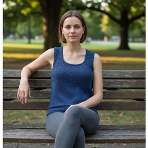 May include: A woman wearing a navy blue tank top with a square neckline and a textured diamond pattern on the upper chest. She is sitting on a wooden park bench, wearing gray pants. The background shows a park with trees.