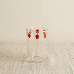 Könnte beinhalten: Ein klares Glas mit zylindrischer Form. Das Glas ist mit einem Muster aus roten Erdbeeren mit grünen Stielen am oberen Rand verziert. Das Glas steht auf einer strukturierten Oberfläche in neutraler Farbe.