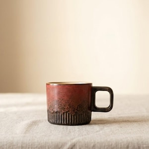 Peut inclure: Une tasse en céramique avec une finition dégradée rouge foncé et marron. La tasse a une anse carrée et une section inférieure texturée avec des lignes verticales. L'intérieur est de couleur marron clair.