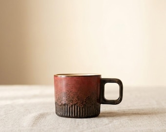 May include: A ceramic mug with a dark red and brown gradient finish. The mug has a square handle and a textured lower section with vertical lines. The interior is a lighter brown color.