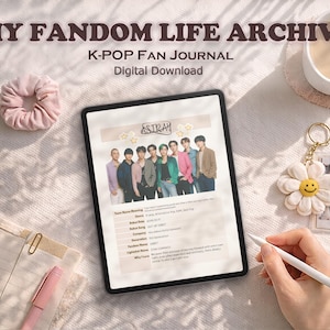 May include: A digital K-Pop fan journal on a tablet, titled "My Fandom Life Archive." The tablet shows a photo of a K-Pop group. A scrunchie, a flower keychain, and a cup of coffee are also visible.