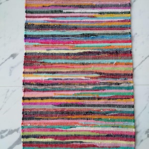 May include: A rectangular, multi-colored rag rug with horizontal stripes. The rug features a variety of colors including pink, red, green, yellow, and black. The rug has a fringed edge on the top and bottom. The rug is made of woven fabric.