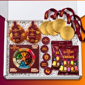 May include: A gift box containing The Traitors themed items: two mesh bags of milk chocolate coins, three gold-coloured plastic medals with maroon lanyards, five maroon plastic tokens, a spin-to-play jelly bean game, and two bags of fruit chews.