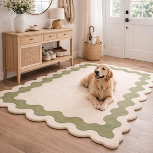 May include: A rectangular area rug featuring a cream-colored center and a wide, wavy sage green border with a scalloped edge. The rug is positioned on a light wood floor, with a golden retriever dog lying in the center of the rug's surface.
