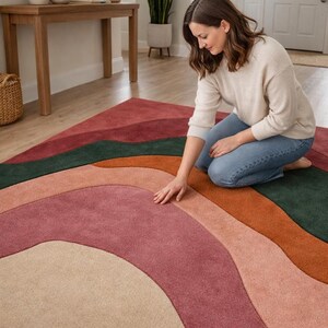 Könnte beinhalten: Ein mehrfarbiger Teppich mit wellenförmigem Design. Der Teppich hat Farbtöne von Rot, Grün, Orange, Rosa und Beige. Der Teppich liegt auf einem Holzboden in einem hellen Raum.