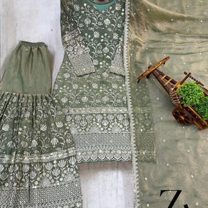Pu&ograve; includere: Completo ricamato in verde salvia composto da tre pezzi. Il set include una tunica a maniche lunghe, pantaloni a gamba larga e una sciarpa trasparente. La tunica e i pantaloni presentano ricami floreali intricati con dettagli argentati. La sciarpa ha un delicato bordo argentato.