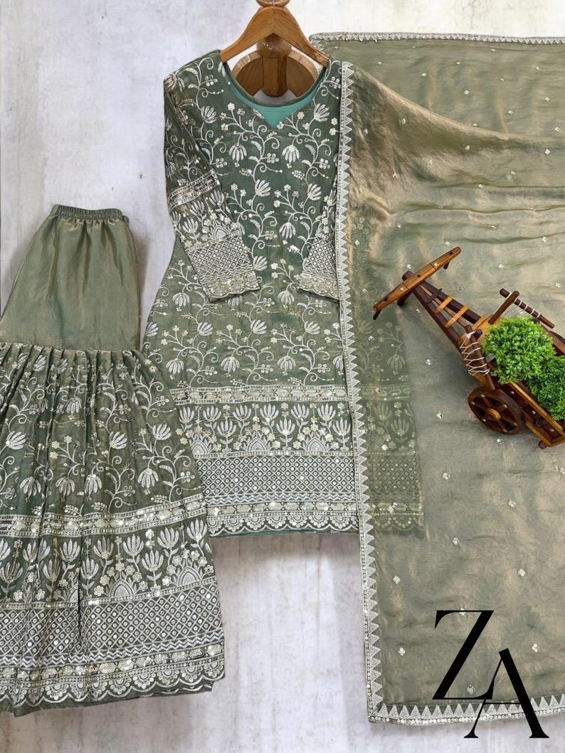 Pu&ograve; includere: Completo ricamato in verde salvia composto da tre pezzi. Il set include una tunica a maniche lunghe, pantaloni a gamba larga e una sciarpa trasparente. La tunica e i pantaloni presentano ricami floreali intricati con dettagli argentati. La sciarpa ha un delicato bordo argentato.