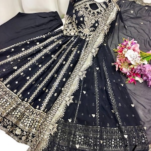 May include: A black formal dress with intricate gold embroidery and embellishments. The dress features a keyhole neckline, long sleeves, and a flowing skirt. A matching black scarf and pants are included. A bouquet of flowers is visible.