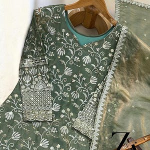 Pu&ograve; includere: Completo formale ricamato verde salvia. Il set include una tunica a maniche lunghe con ricami floreali intricati e una sciarpa trasparente abbinata. Il ricamo &egrave; in filo d'argento.