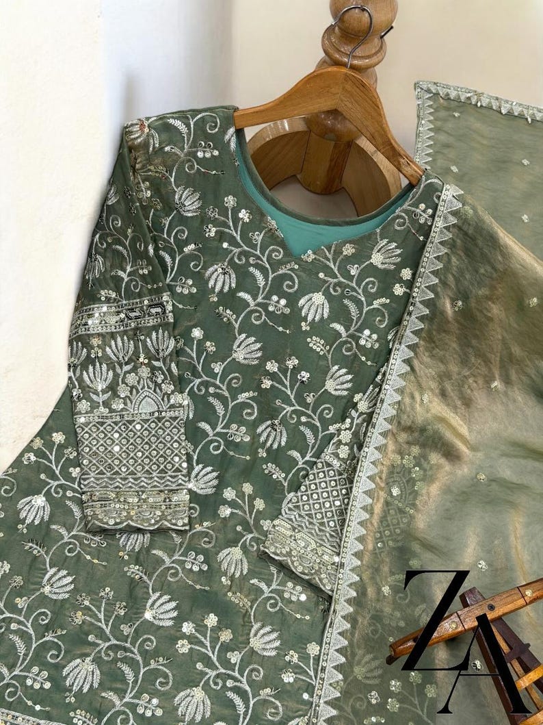 Pu&ograve; includere: Completo formale ricamato verde salvia. Il set include una tunica a maniche lunghe con ricami floreali intricati e una sciarpa trasparente abbinata. Il ricamo &egrave; in filo d'argento.