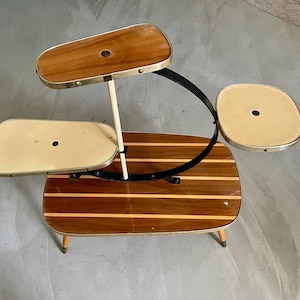 Puede incluir: Un soporte para plantas de estilo moderno de mediados de siglo con tres niveles de madera. El soporte presenta una base de madera oscura con rayas de madera más claras, un soporte de metal negro curvado y adornos de color latón. El soporte mide aproximadamente 76 cm de alto.