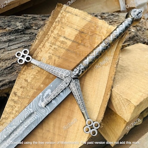 May include: A silver-toned sword featuring a Damascus steel blade with a wavy pattern. The hilt includes an intricate crossguard with scrollwork, a textured grip, and a pommel shaped like a lion head with four-ringed quillon terminals.