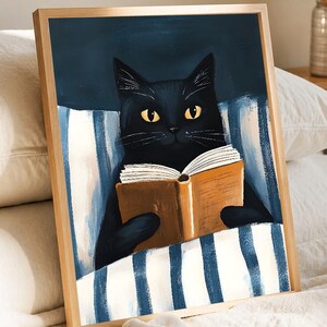 Peut inclure: Impression artistique encadrée d'un chat noir lisant un livre au lit. Le chat aux yeux jaunes est sous une couverture à rayures bleues et blanches. L'œuvre est dans un cadre en bois, sur fond bleu foncé.