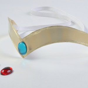 May include: A gold-colored headband with a blue gem and two loose gems, one pink and one red.