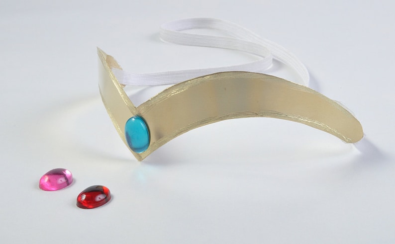 May include: A gold-colored headband with a blue gem and two loose gems, one pink and one red.