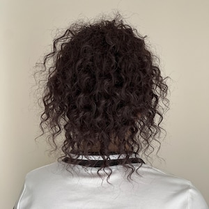 May include: A person's head with dark brown, tightly curled hair. The person is wearing a white shirt with black stripes on the sleeves and around the collar.