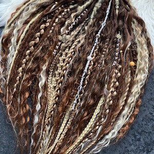 May include: A collection of brown, blonde, and auburn dreadlocks, some with decorative beads and charms. The dreadlocks are arranged in a fan shape, with a variety of textures and styles, including braids and twists. A brown ribbon is tied at the top.