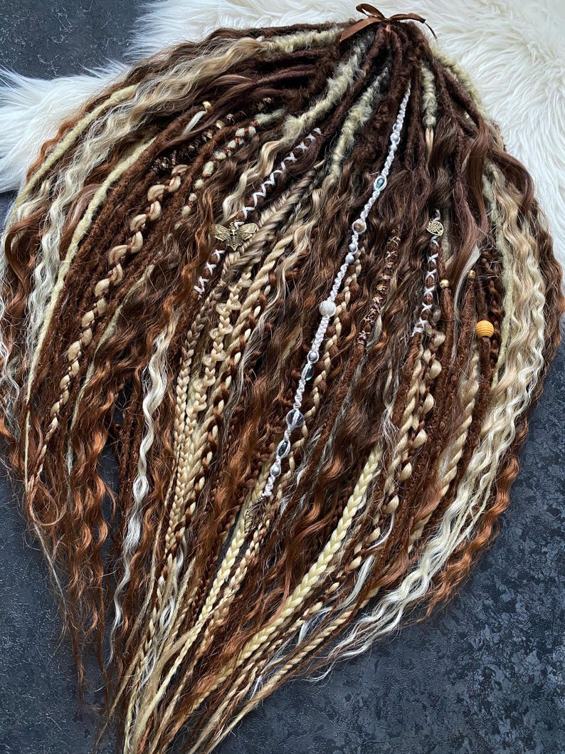 May include: A collection of brown, blonde, and auburn dreadlocks, some with decorative beads and charms. The dreadlocks are arranged in a fan shape, with a variety of textures and styles, including braids and twists. A brown ribbon is tied at the top.