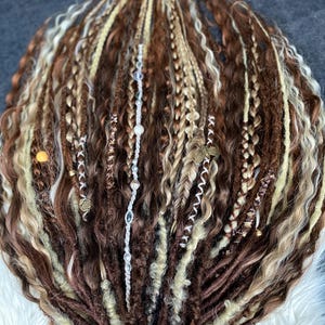 May include: A collection of brown, blonde, and light brown dreadlocks, some with braids and decorative beads. The dreadlocks are arranged in a fan shape, with a ribbon at the base.