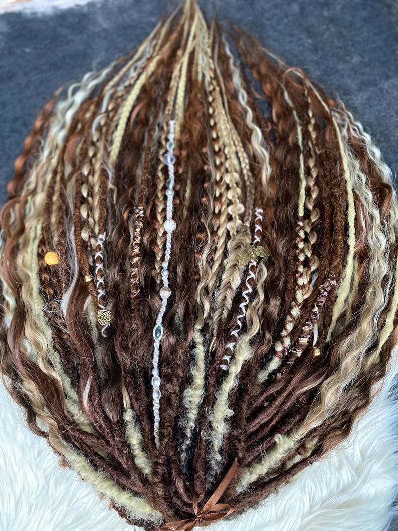 May include: A collection of brown, blonde, and light brown dreadlocks, some with braids and decorative beads. The dreadlocks are arranged in a fan shape, with a ribbon at the base.