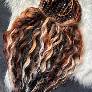 May include: A set of handmade dreadlocks in a variety of colors, including black, brown, blonde, and red. The dreadlocks are styled with a brown ribbon and orange bow. The hair is wavy and appears to be made of synthetic fibers.