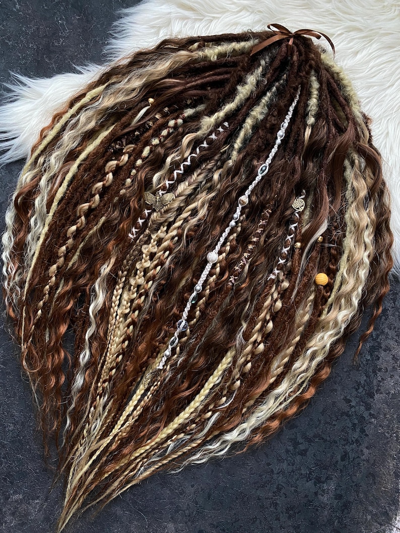 May include: A collection of brown, blonde, and white dreadlocks, some with decorative beads and charms. The dreadlocks are styled with various textures, including braids and wavy sections. A brown ribbon is tied at the top.