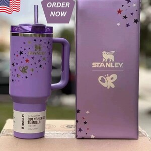 May include: A purple Stanley Quencher H2.0 FlowState tumbler with a handle, straw, and lid. The tumbler is decorated with star and butterfly designs. The box next to it has the Stanley logo and matching star designs. The text "ORDER NOW" is in the top right corner.