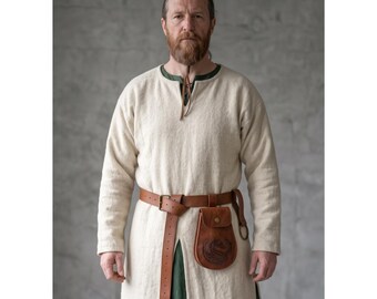 Peut inclure: Une tunique blanc cassé à manches longues avec une encolure ronde et une petite fente, portée sur un vêtement vert foncé. Une ceinture en cuir marron avec une boucle en métal est fixée à la taille, avec une pochette en cuir marron embossée.