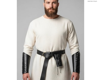 Peut inclure: Tunique crème avec une ceinture en cuir noir et des protège-bras assortis. Les protège-bras présentent un laçage. La ceinture a une boucle dorée et une petite pochette. Le logo "SINISTER STRAPS" est dans le coin supérieur droit.