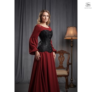 Puede incluir: Una mujer con un vestido burdeos de manga larga y un corsé negro. El corsé tiene un diseño floral y se ata en la espalda. El conjunto es de estilo gótico o victoriano.