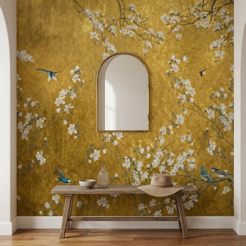 May include: A room interior featuring a gold-toned wall with a floral and bird design. A wooden bench holds a hat, bowl, and glass bottle. A gold-framed mirror hangs on the wall. The room has a warm, inviting atmosphere.